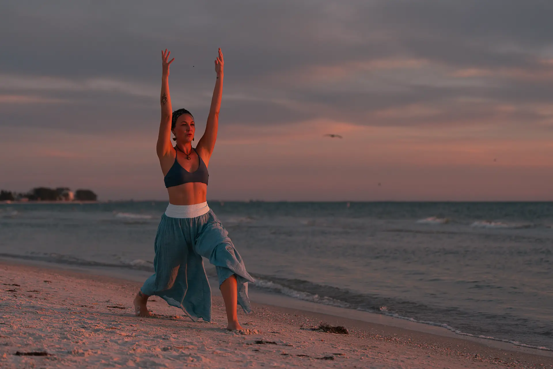 Jaime in a warrior pose on the beach at sunset