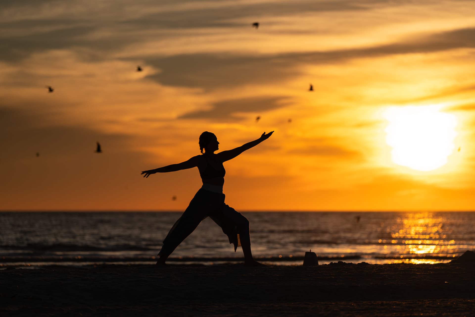 Jaime in warrior two silhouetted against a golden beach sunset