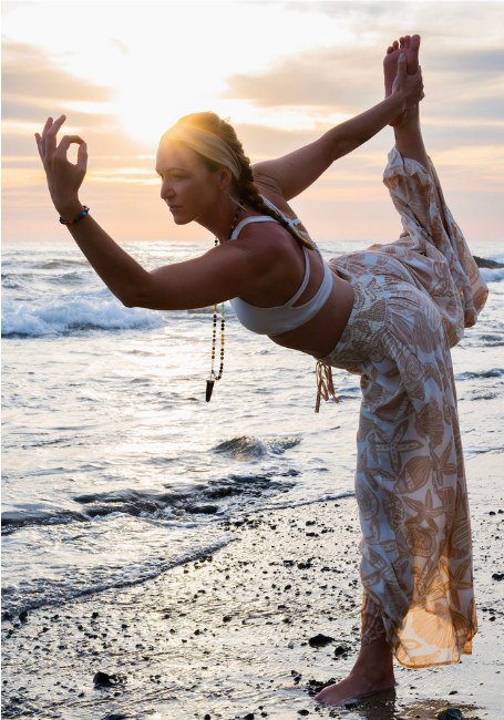 Jaime practising a standing yoga pose on a pebble beach at sunset